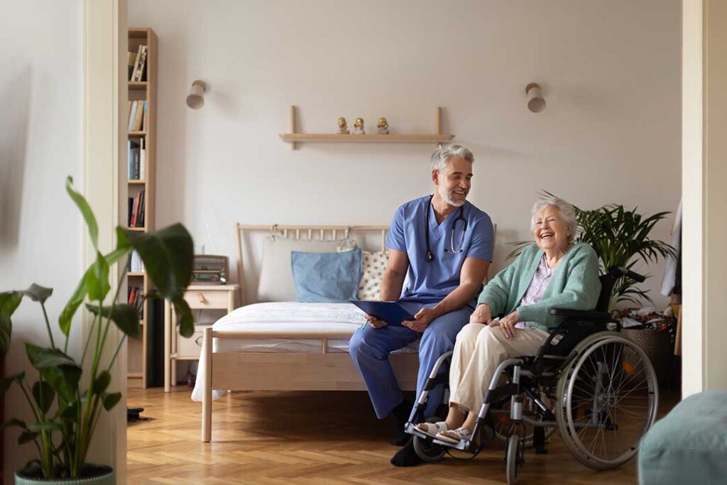 Older resident uses a tablet with a caregiver beside a comfortable assisted living room.